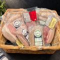 A wicker basket filled with packaged cured meats from Parker's, including British back bacon, and sausages.
