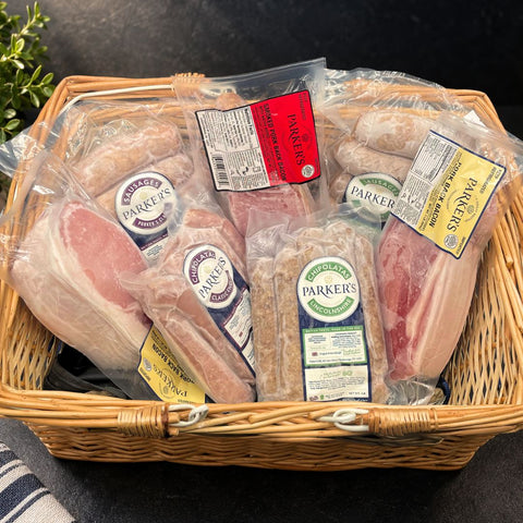 A wicker basket filled with packaged cured meats from Parker's, including British back bacon, and sausages.
