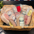 A wicker basket filled with packaged cured meats from Parker's, including British back bacon, and sausages.